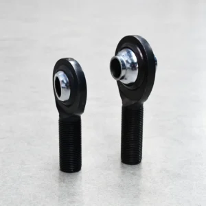 Two black high-misalignment rod ends (PCM and PCYM) standing upright, designed for off-road suspension systems.