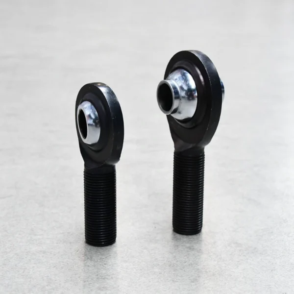 Two black high-misalignment rod ends (PCM and PCYM) standing upright, designed for off-road suspension systems.