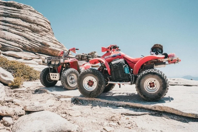 Two red ATVs parked on rocky terrain with a clear sky in the background, one with a helmet mounted on the back, showcasing off-road adventure.