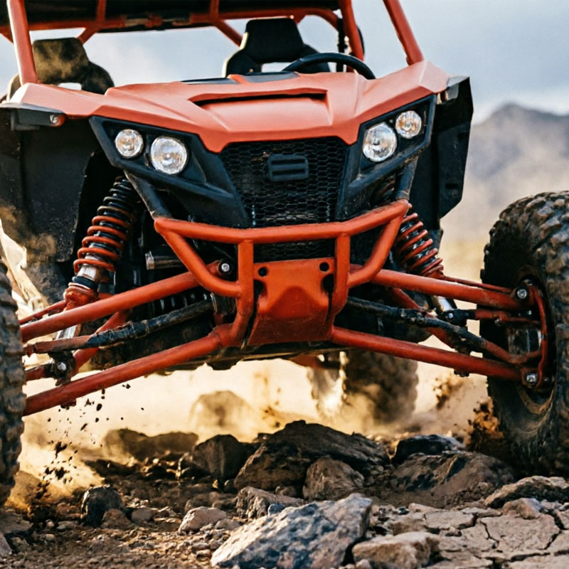 Front view of a red off-road buggy navigating a rocky dirt trail with dust and exposed suspension.