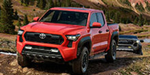 Red Toyota pickup truck off-roading on a dirt trail with rugged hills in the background