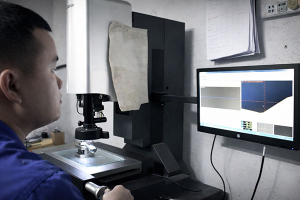 Lab technician operating a precision microscope connected to a monitor for image analysis