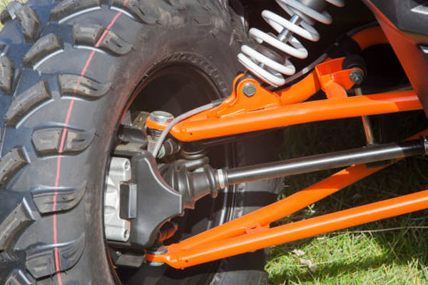 Close-up of an orange bicycle rear suspension with a white coil spring and a knobby off-road tire.