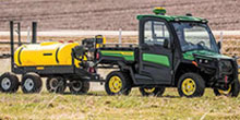 Green and black agricultural tractor with a bright yellow liquid tank and spray rig, parked in a field (crop spraying equipment)