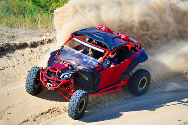 Red off-road dune buggy kicking up dust while navigating a sandy hill at high speed.