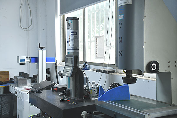 Industrial testing machine and control panel on a black workbench by a window in a lab environment.