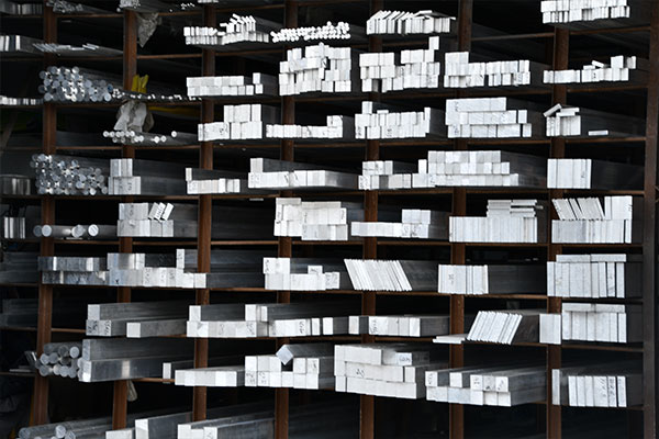 Rows of silver metal rectangular bars and tubes neatly stacked on wooden shelves in a warehouse.
