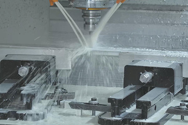 CNC milling machine in operation with coolant spray hitting the cutting tool and metal workpiece, with clamps securing the workpiece.