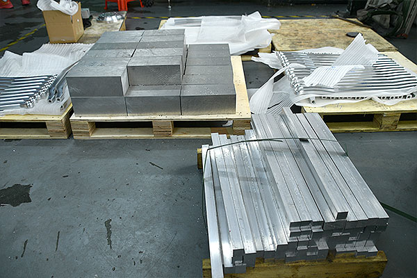 Stacks of rectangular metal blocks on wooden pallets in a warehouse setting, ready for transport or processing.