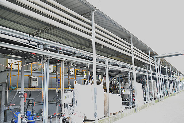 Industrial facility with metal pipes, valves, and machinery under a covered outdoor walkway.