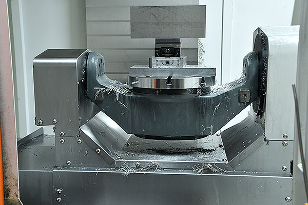 Industrial milling machine spindle clamping a circular workpiece in a fixture with metal chips around the area