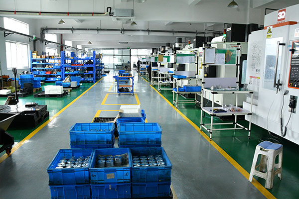 Factory floor with blue plastic crates stacked in the foreground and machining stations along the aisles.
