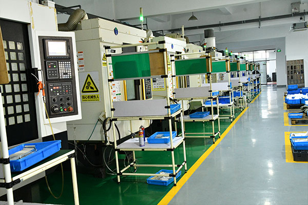 Row of industrial machines along a polished factory floor with control panels, yellow safety lines, and blue bins awaiting parts